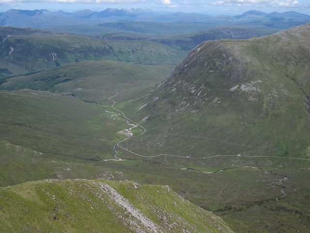 looking down towards a stream and a track which wind across a grey-green valley between winding hills